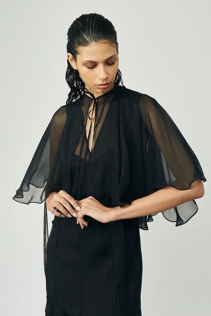 Portfolio Lorenzo Berni_095 - Lorenzo Berni Woman in a black sheer cape blouse tying a black ribbon at the neckline, looking down.